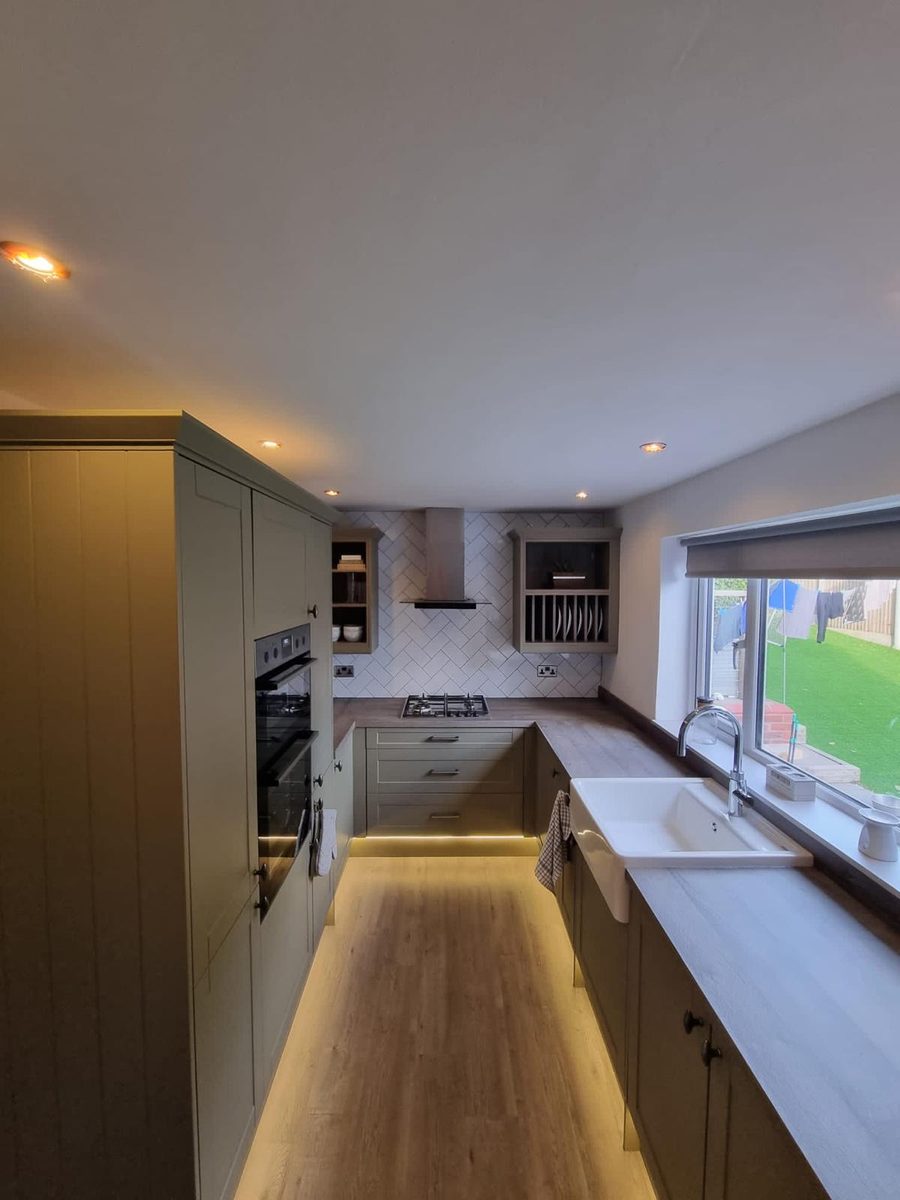 Sage green shaker kitchen with a wood worktop, Belfast sink and plinth lighting